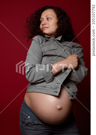 Attractive African American young pregnant woman with naked belly, wearing stylish casual denim blazer, isolated on red 105107792