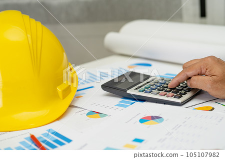 Asian engineer with architectural house plan project blueprint, graph and yellow helmet and engineering construction tools. 105107982