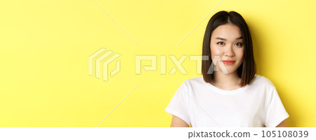 Close up of beautiful asian woman with casual makeup, raising eyebrow and looking intrigued at camera, standing curious over yellow background Close up of beautiful asian woman with casual makeup, raising eyebrow and looking intrigued at camera, standing curious over yellow background 105108039