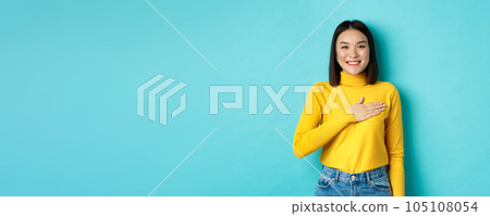 Image of proud smiling asian woman holding hand on heart, showing respect to national anthem, standing over blue background 105108054