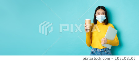 covid-19, health care and quarantine concept. Asian girl student in medical mask standing with laptop and coffee from cafe, standing over blue background covid-19, health care and quarantine concept. Asian girl student in medical mask standing with laptop and coffee from cafe, standing over blue background 105108105