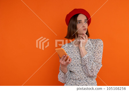 Pensive thoughtful adult woman wearing elegant dress and red beret holding smartphone. Pensive thoughtful adult woman wearing elegant dress and red beret holding smartphone. 105108256