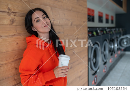Portrait of young woman standing in the self-service public laundry. 105108264