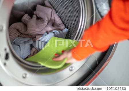 Woman washing dirty clothes, cleaning washing machine with rag in the laundry room. Woman washing dirty clothes, cleaning washing machine with rag in the laundry room. 105108280