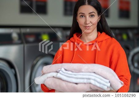 Laundry service. Brunette adult woman holding washed towels in public laundry. 105108290