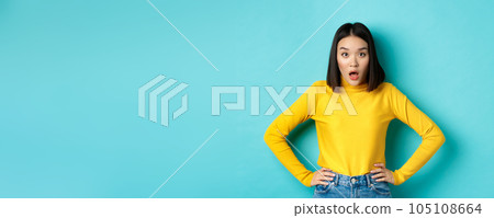 Portrait of surprised asian woman drop jaw, listening to big news, looking amazed at camera, standing in yellow sweater against blue background Portrait of surprised asian woman drop jaw, listening to big news, looking amazed at camera, standing in yellow sweater against blue background 105108664