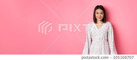 Beautiful asian lady smiling at camera, wearing cute romantic dress, standing over pink background Beautiful asian lady smiling at camera, wearing cute romantic dress, standing over pink background 105108707