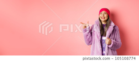 Happy senior asian woman smiling, pointing finger left and looking satisfied, checking out special promotion, pink background Happy senior asian woman smiling, pointing finger left and looking satisfied, checking out special promotion, pink background 105108774