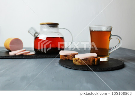 still life of tea breakfast tea sausage sandwiches on a tray tea in a glass cup and glass teapot on a gray background with space for text and copyspace still life of tea breakfast tea sausage sandwiches on a tray tea in a glass cup and glass teapot on a gray background with space for text and copyspace 105108863