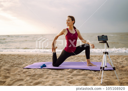 Online training. Sporty woman yoga coach records video online training on beach. Sport, Blogging. Online training. Sporty woman yoga coach records video online training on beach. Sport, Blogging. 105108920