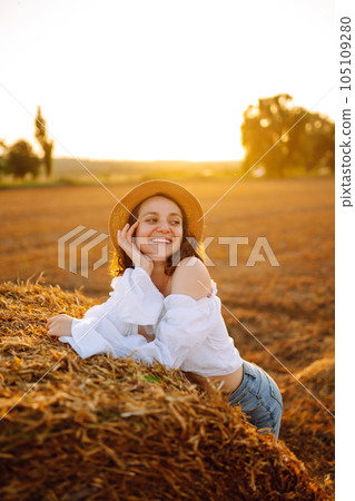 Happy woman near haystack at sunset. Fashion concept. Nature, vacation, relax and lifestyle. 105109280