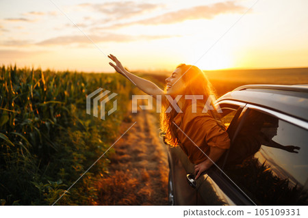 Happy woman outstretches her arms while sticking out car window. Lifestyle, travel, tourism, nature. 105109331