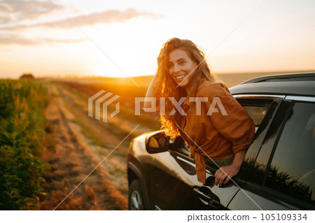 Happy woman outstretches her arms while sticking out car window. Lifestyle, travel, tourism, nature. 105109334