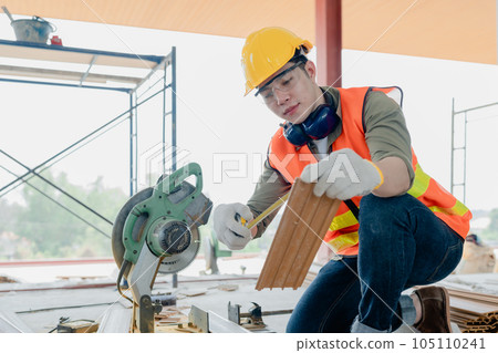Structural worker dressed in safety gear and hard hat doing construction and using circular saw to work Structural worker dressed in safety gear and hard hat doing construction and using circular saw to work 105110241