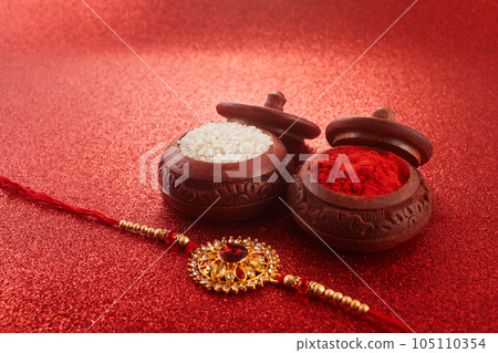 Raksha Bandhan. Rakhi string, Rice Grains and Kumkum on red background. 105110354