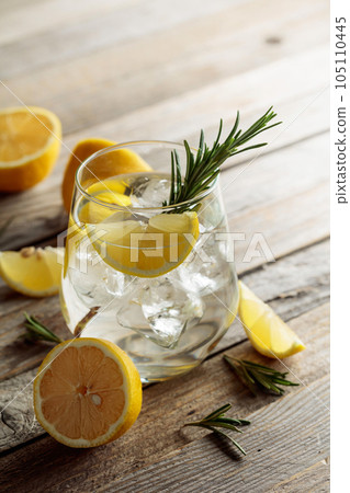 Gin tonic with ice, rosemary, and lemon slices on an old wooden table. Gin tonic with ice, rosemary, and lemon slices on an old wooden table. 105110445