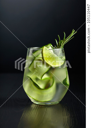 Gin tonic with ice, rosemary, lime, and cucumber in frosted glass on a black background. 105110447
