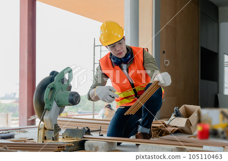 Structural worker dressed in safety gear and hard hat doing construction and using circular saw to work 105110463