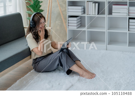 Happy young woman wear headphone with using tablet in living room on sofa. Young happy woman lie playing smart tablet at home. Beautiful young asian women using tablet computer Happy young woman wear headphone with using tablet in living room on sofa. Young happy woman lie playing smart tablet at home. Beautiful young asian women using tablet computer 105110488