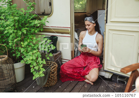 Happy hippie girl are having a good time with cup of tea in camper trailer. Holiday, vacation, trip concept. Happy hippie girl are having a good time with cup of tea in camper trailer. Holiday, vacation, trip concept. 105110767