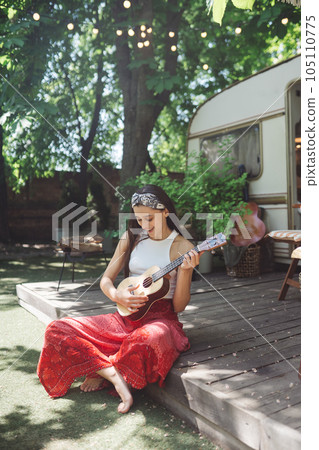 Happy hippie girl is having a good time with playing on guitar in camper trailer. Holiday, vacation, trip concept. Happy hippie girl is having a good time with playing on guitar in camper trailer. Holiday, vacation, trip concept. 105110775