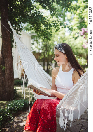 Happy hippie girl is reading a book in hammock having a good time in camper trailer. Holiday, vacation, trip concept. Happy hippie girl is reading a book in hammock having a good time in camper trailer. Holiday, vacation, trip concept. 105110824