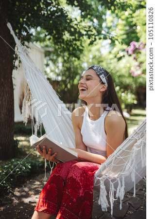 Happy hippie girl is reading a book in hammock having a good time in camper trailer. Holiday, vacation, trip concept. Happy hippie girl is reading a book in hammock having a good time in camper trailer. Holiday, vacation, trip concept. 105110826