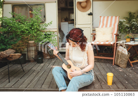 Happy hippie girl is having a good time with playing on guitar in camper trailer. Holiday, vacation, trip concept. Happy hippie girl is having a good time with playing on guitar in camper trailer. Holiday, vacation, trip concept. 105110863