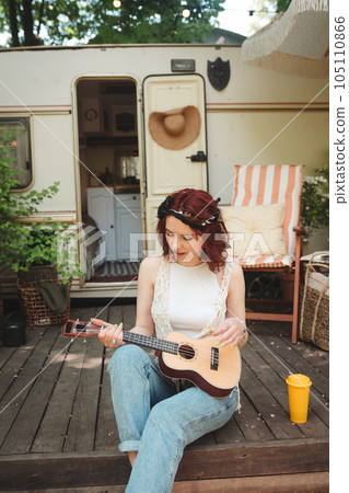 Happy hippie girl is having a good time with playing on guitar in camper trailer. Holiday, vacation, trip concept. Happy hippie girl is having a good time with playing on guitar in camper trailer. Holiday, vacation, trip concept. 105110866