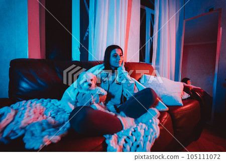 Beautiful young girl at home in a dark room playing with her dog and sits in front of a monitor or TV. Beautiful young girl at home in a dark room playing with her dog and sits in front of a monitor or TV. 105111072