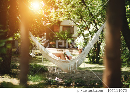 Happy hippie girl is reading a book in hammock having a good time in camper trailer. Holiday, vacation, trip concept. Happy hippie girl is reading a book in hammock having a good time in camper trailer. Holiday, vacation, trip concept. 105111073