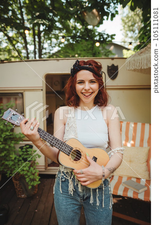 Happy hippie girl is having a good time with playing on guitar in camper trailer. Holiday, vacation, trip concept. Happy hippie girl is having a good time with playing on guitar in camper trailer. Holiday, vacation, trip concept. 105111081