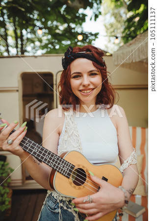 Happy hippie girl is having a good time with playing on guitar in camper trailer. Holiday, vacation, trip concept. Happy hippie girl is having a good time with playing on guitar in camper trailer. Holiday, vacation, trip concept. 105111137