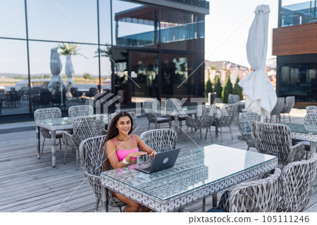 Cute young woman in swimsuit working on laptop sitting on terrace on the beach 105111246