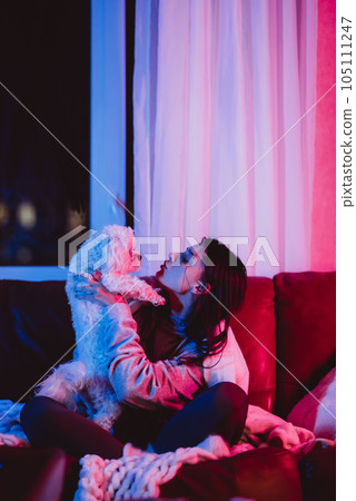 Beautiful young girl watching movie at home in a dark room with a popcorn bucket and playing with her dog and sits in front of a monitor or TV. Beautiful young girl watching movie at home in a dark room with a popcorn bucket and playing with her dog and sits in front of a monitor or TV. 105111247