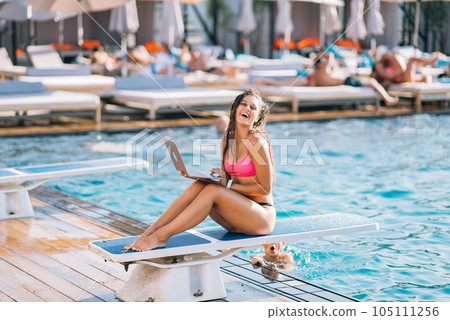 Cute young woman in swimsuit smiling sunbathing with a laptop in a pool 105111256