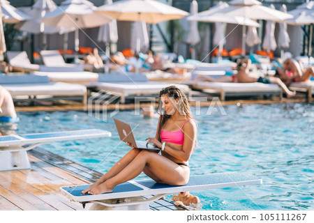Cute young woman in swimsuit sunbathing with a laptop in a pool 105111267