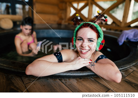 Young girls in bikinis bathing in an outdoor bathtub on winter holidays 105111510
