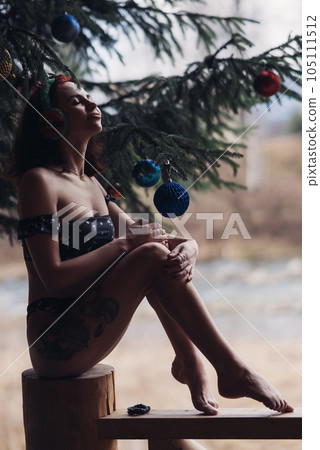 Beautiful girl in bikini sitting against of snow-covered trees in winter Beautiful girl in bikini sitting against of snow-covered trees in winter 105111512