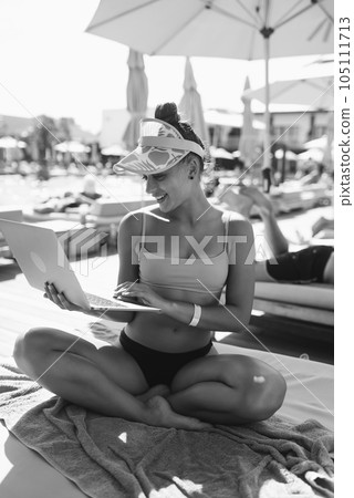 black and white portrait of beautiful girl in bikini is working with a laptop sunbathing on the beach 105111713