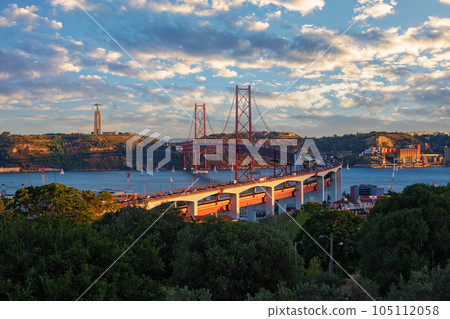 View of Lisbon view from Miradouro do Bairro do Alvito tourist viewpoint of Tagus river, traffic on 25th of April Bridge, and Christ the King statue at sunset. Lisbon, Portugal 105112058