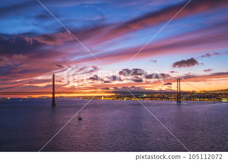 View of 25 de Abril Bridge famous tourist landmark of Lisbon connecting Lisboa and Almada on Setubal Peninsula over Tagus river in the evening twilight with boats. Lisbon, Portugal View of 25 de Abril Bridge famous tourist landmark of Lisbon connecting Lisboa and Almada on Setubal Peninsula over Tagus river in the evening twilight with boats. Lisbon, Portugal 105112072