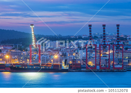 View of Lisbon port with moored sea container ship with port cranes in the evening twilight over Tagus river. Lisbon, Portugal 105112078