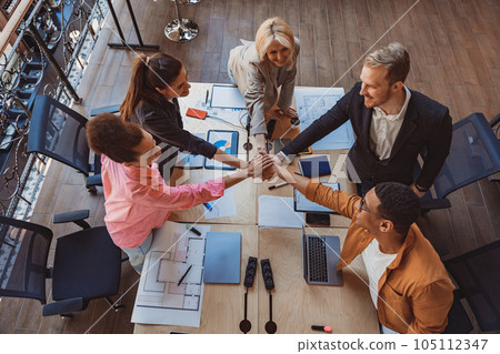 Top view of colleagues putting their arms in centre standing at modern office. Community concept Top view of colleagues putting their arms in centre standing at modern office. Community concept 105112347