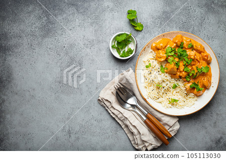 Traditional Indian dish chicken curry with basmati rice and fresh cilantro on rustic white plate on gray concrete table background from above. Indian dinner meal 105113030