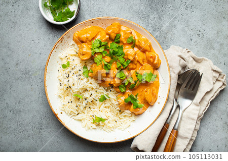 Traditional Indian dish chicken curry with basmati rice and fresh cilantro on rustic white plate on gray concrete table background from above. Indian dinner meal 105113031