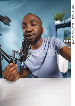 Streamer recording video for internet vlog and speaking with subscribers while holding camera. Young african american blogger talking in mic while streaming online portrait 105115863