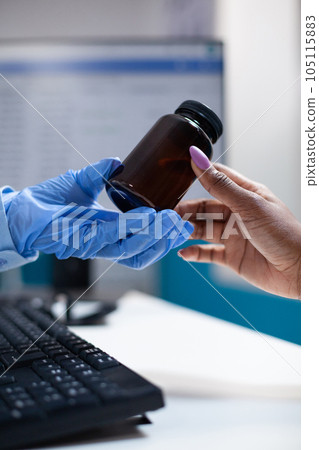 Doctor offering medicine pill bottle to patient during appointment. Clinical consultation by doctor with protective medical gloves prescribing medicine inside hospital office, closeup 105115883