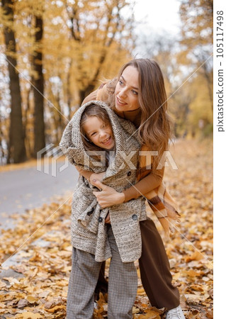 Young woman and little girl in autumn forest. Woman hugging her daughter. Girl wearing mother's oversize jacket. 105117498