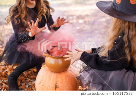 Mother witch and her daughter making a potion in autumn forest. Mother teach her daughter. Young woman and little girl wearing witches Halloween costumes and cone hats. Mother witch and her daughter making a potion in autumn forest. Mother teach her daughter. Young woman and little girl wearing witches Halloween costumes and cone hats. 105117552
